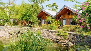 A rustic cabin-style hotel with two wooden buildings, a stone wall, and a pond with vegetation. - Ninh Binh Eco Garden (Tay Hoa Lu)