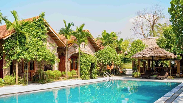 A swimming pool with a clear blue water, surrounded by lush greenery and a thatched-roof pavilion. - Ninh Binh Eco Garden (Tay Hoa Lu)
