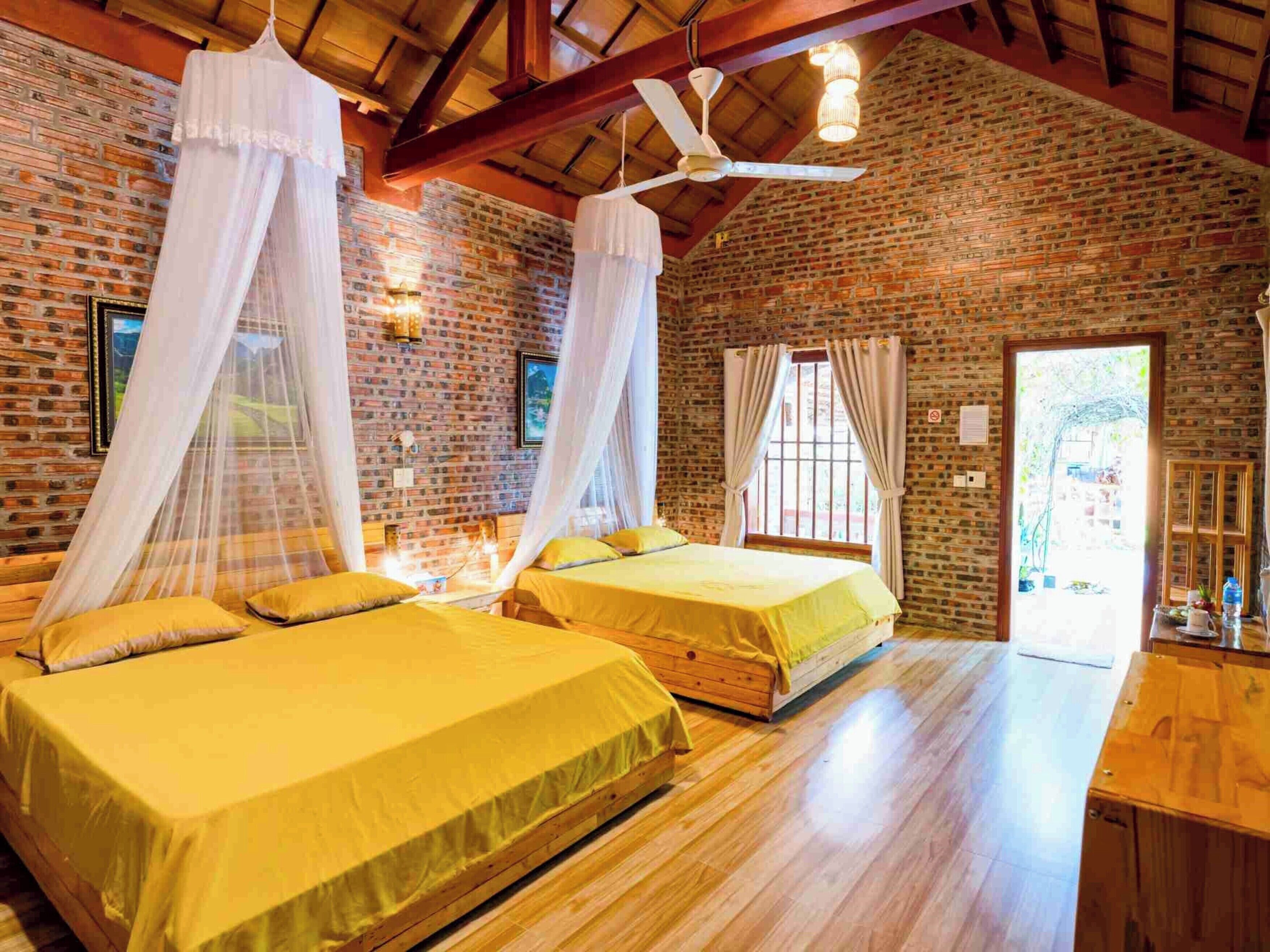 Habitación con dos camas, pisos de madera, paredes de ladrillo y ventilador de techo.