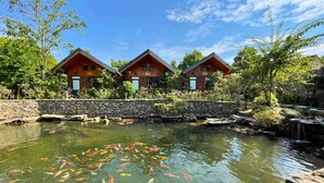 A hotel with three wooden cabins, a koi pond, and a stone wall. - Ninh Binh Eco Garden (Tay Hoa Lu)