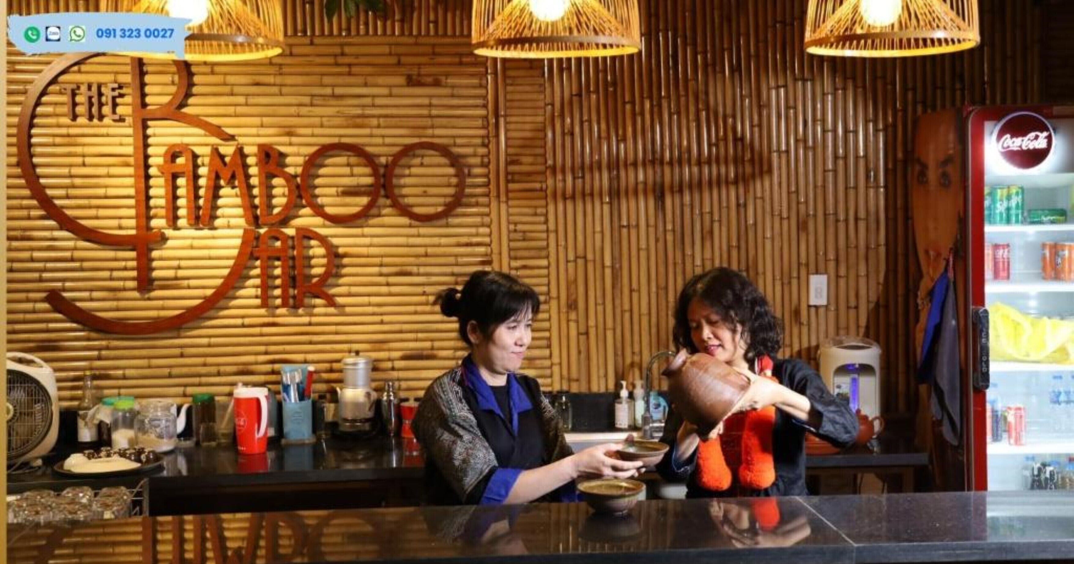 Interior de un restaurante con pared de bambú, un refrigerador de Coca-Cola y una barra con diversos artículos.