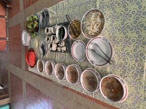 Une table dressée avec différents plats et ustensiles, notamment des bols de soupe, des assiettes de légumes et un saladier de pastèque.