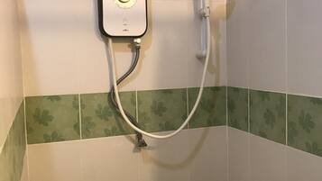 Una unidad de ducha con panel de control y cabezal de ducha de mano, instalada en una pared con azulejos florales verdes.