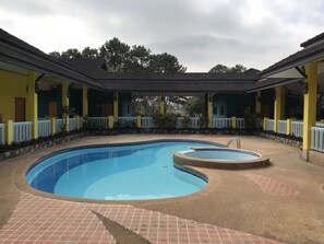 Une piscine dotée d’une plage carrelée, entourée d’une zone abritée aux murs jaunes et bleus, et d’une clôture blanche.