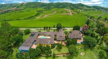 Una extensa propiedad con varias edificaciones, incluyendo una casa principal con piscina, rodeada de campos y colinas verdes y frondosas.