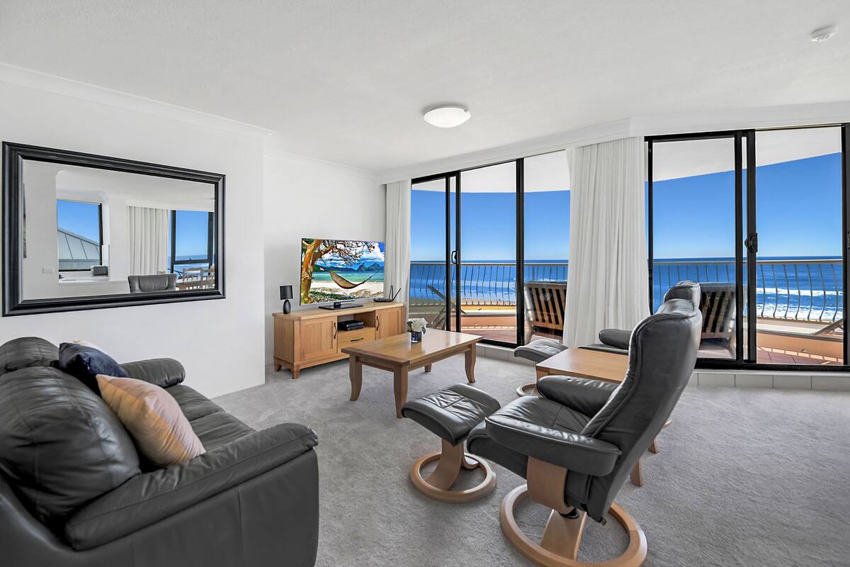 Habitación de hotel moderna con balcón, un amplio ventanal con vistas al mar, zona de estar cómoda y televisor de pantalla plana.