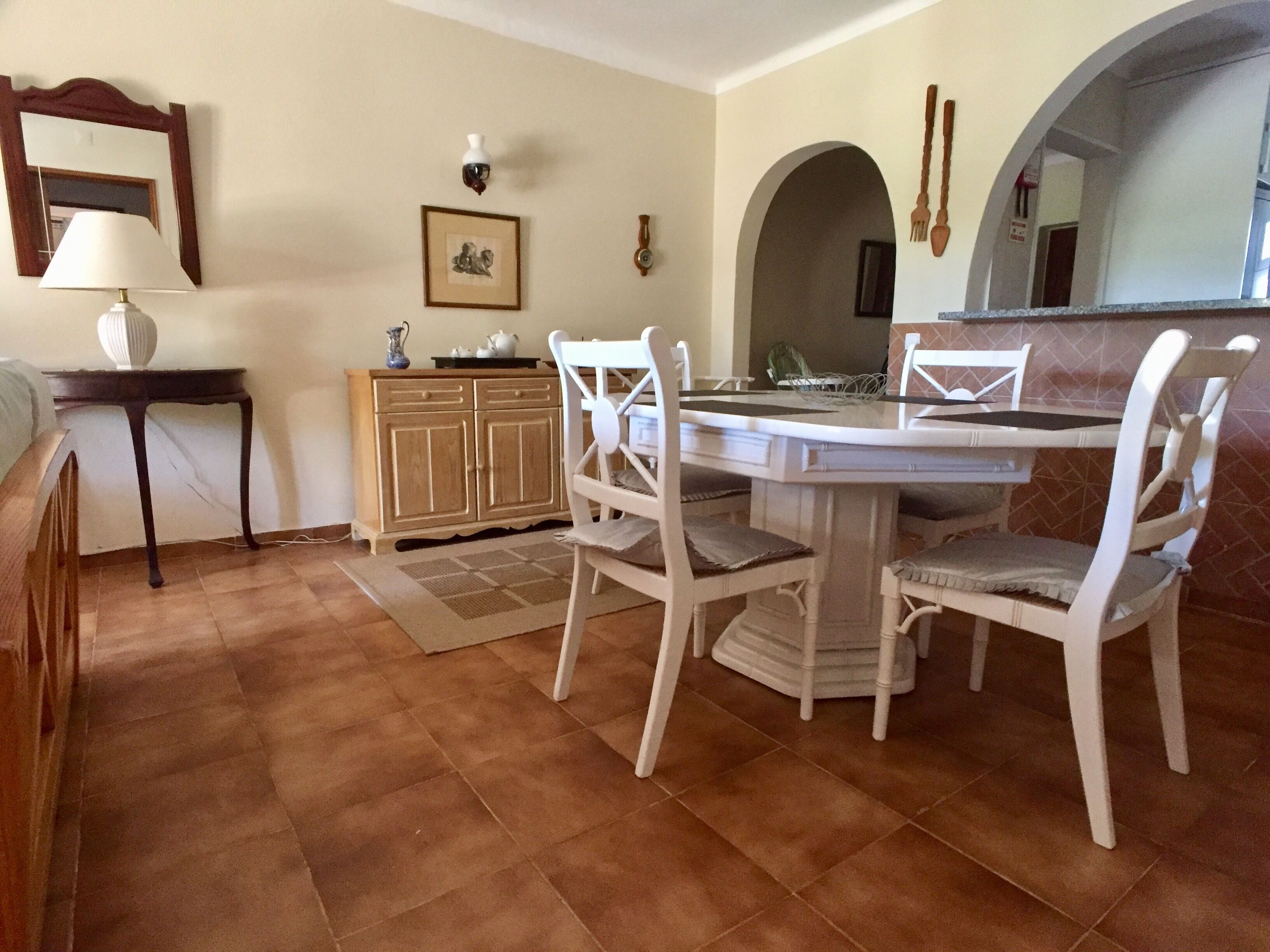 A dining area with a round table, white chairs, a wooden cabinet, and a mirror on the wall.