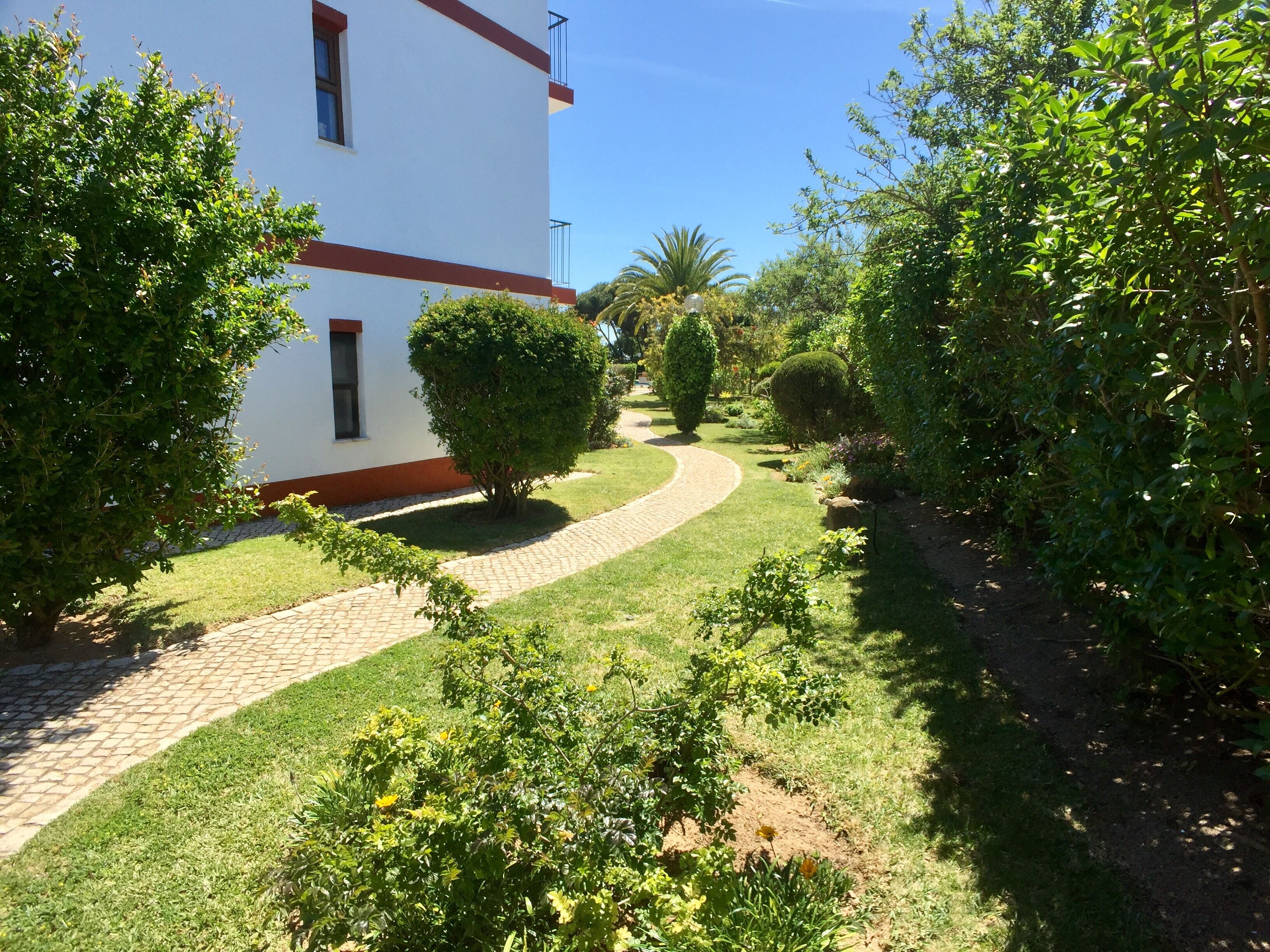A garden pathway leading to a white building with red trim.