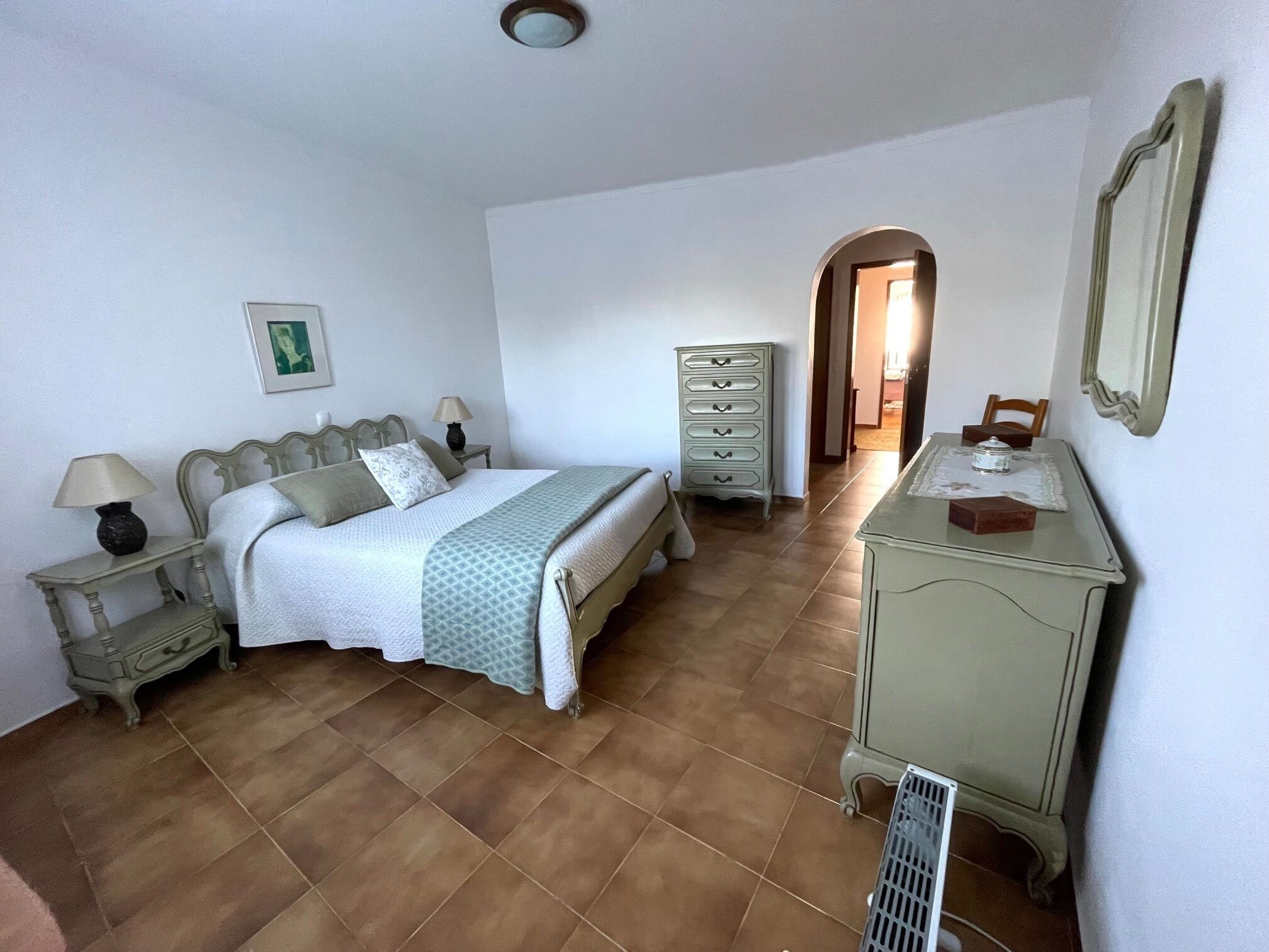 Une chambre à coucher comprenant un lit, une commode, une table de chevet, une lampe et un miroir.