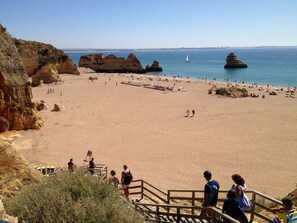 A beach with rocky formations, a clear sky, and a calm sea.