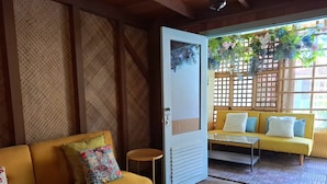 Une pièce avec un canapé jaune, une petite table ronde et une porte qui donne sur une autre pièce, elle aussi dotée d’un canapé jaune et d’une table en verre.
