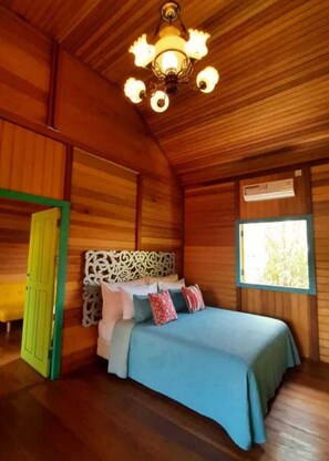 Een houten kamer met een bed, een kroonluchter, een raam en een deur.