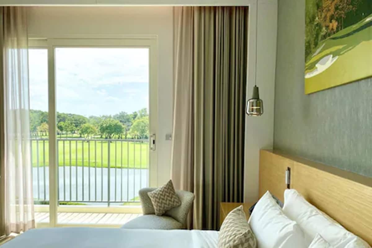 A hotel room with a large bed, a view of a golf course through a sliding glass door, and a painting on the wall.