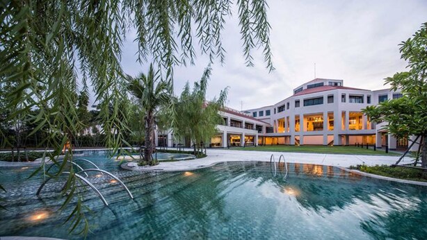 A modern hotel with a swimming pool, surrounded by palm trees and a well-maintained garden. - Eastin Thana City Golf Resort Bangkok (Bang Phli)