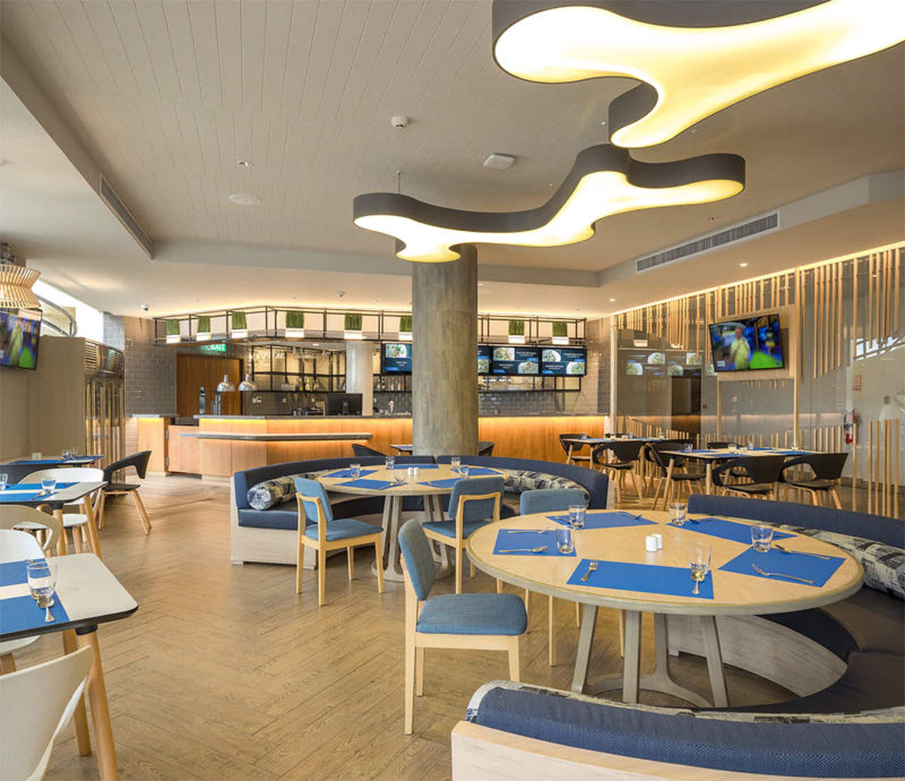 Un restaurant moderne avec des tables rondes et des sièges recouverts d’un tissu bleu.