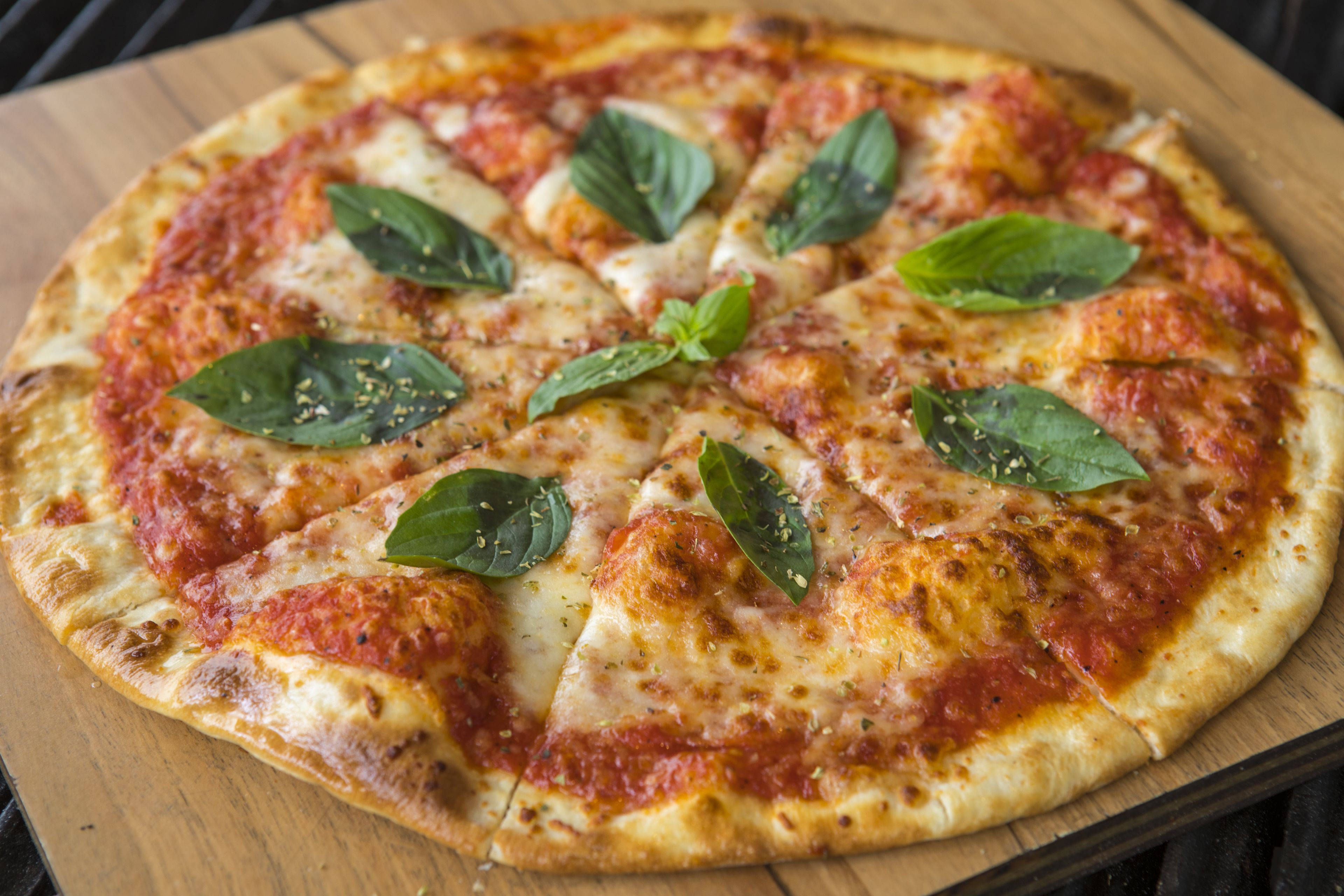 Una pizza con queso y hojas de albahaca sobre una tabla de madera.