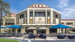 A building with a sign reading "THANA CITY" and outdoor seating with umbrellas. - Eastin Thana City Golf Resort Bangkok (Bang Phli)