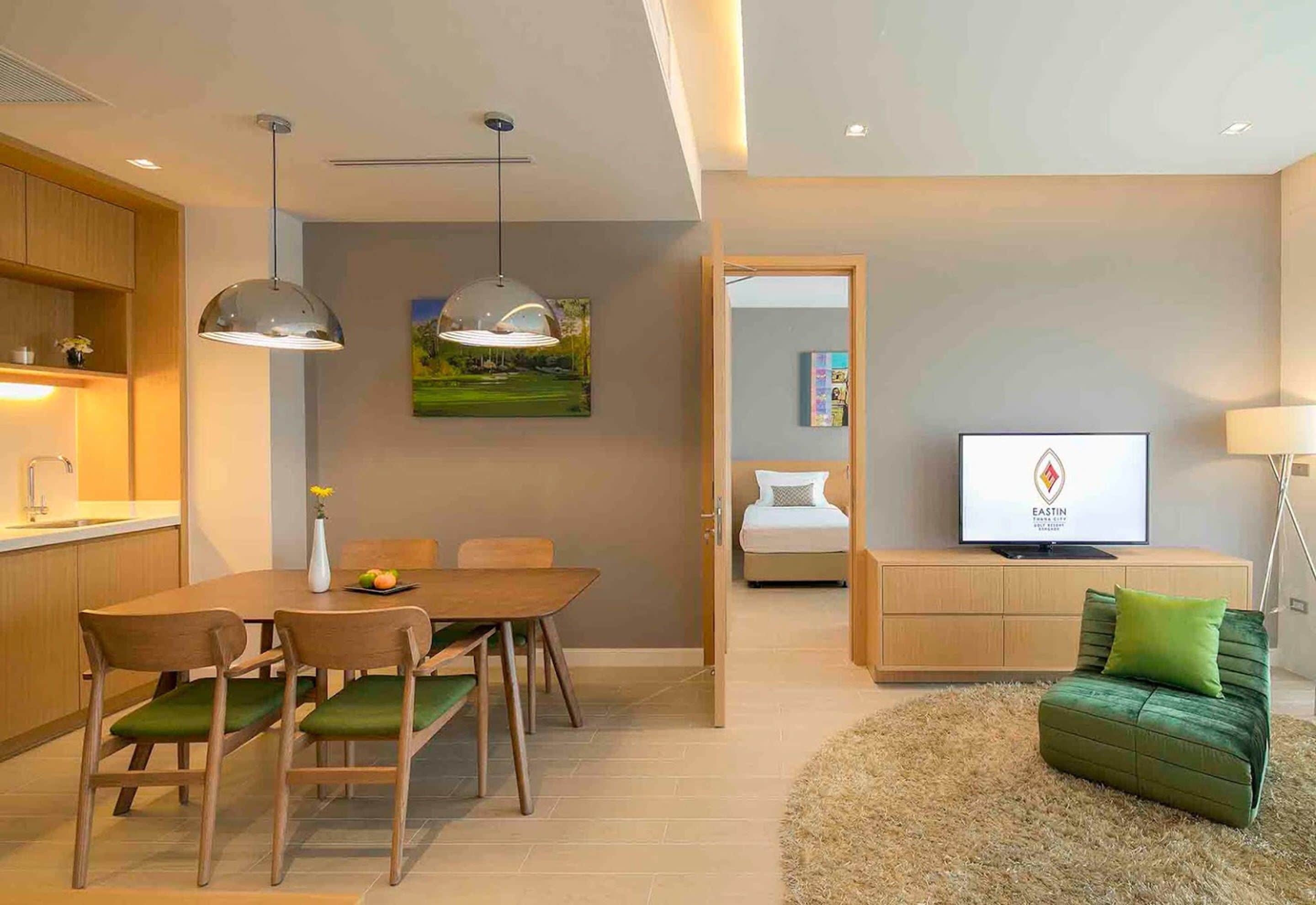 Una sala moderna con un sofá verde, un comedor con muebles de madera, un televisor sobre un mueble de madera y un cuadro en la pared.