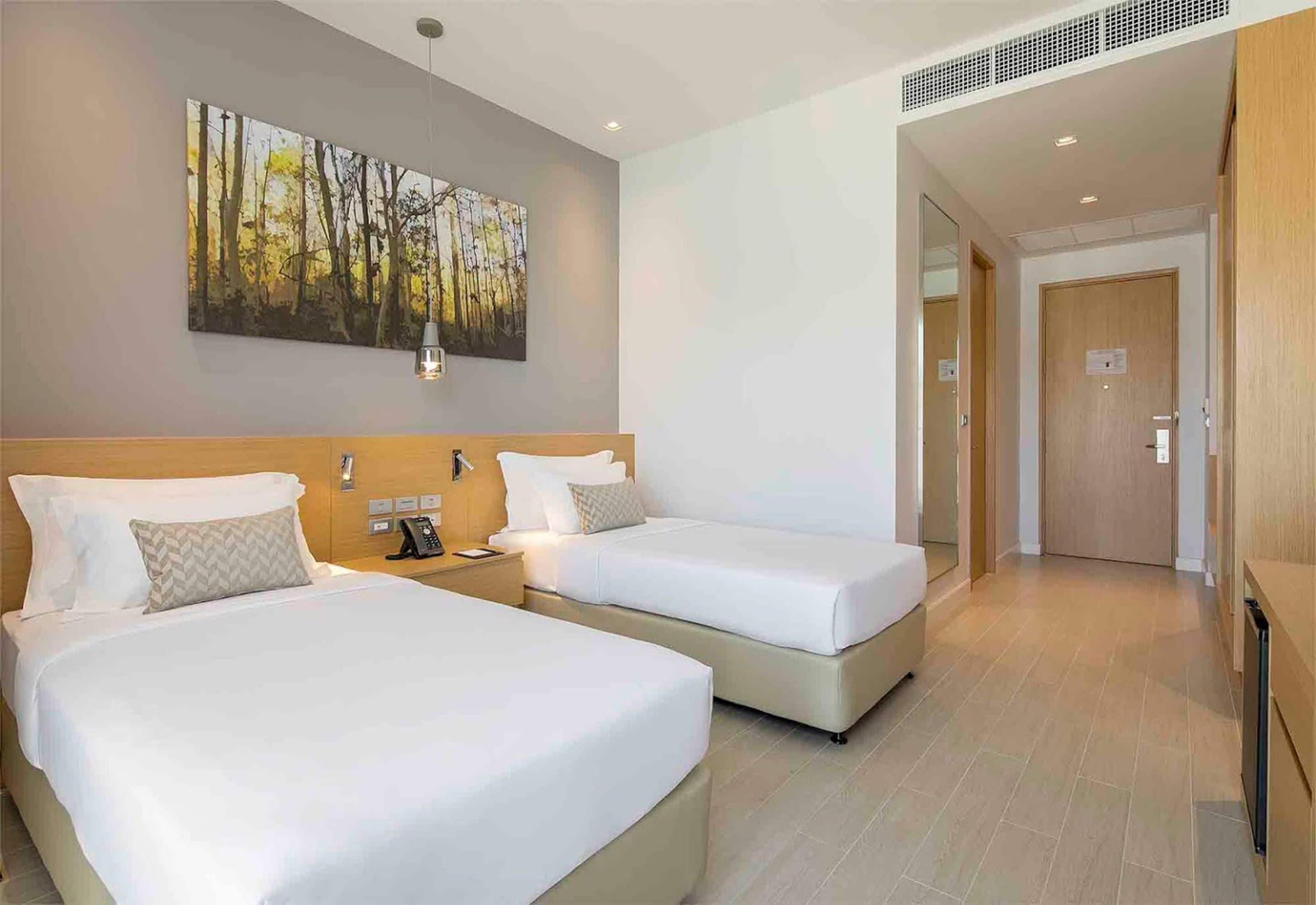 A hotel room with two beds, a painting on the wall, a phone on the nightstand, and a door leading to another room.
