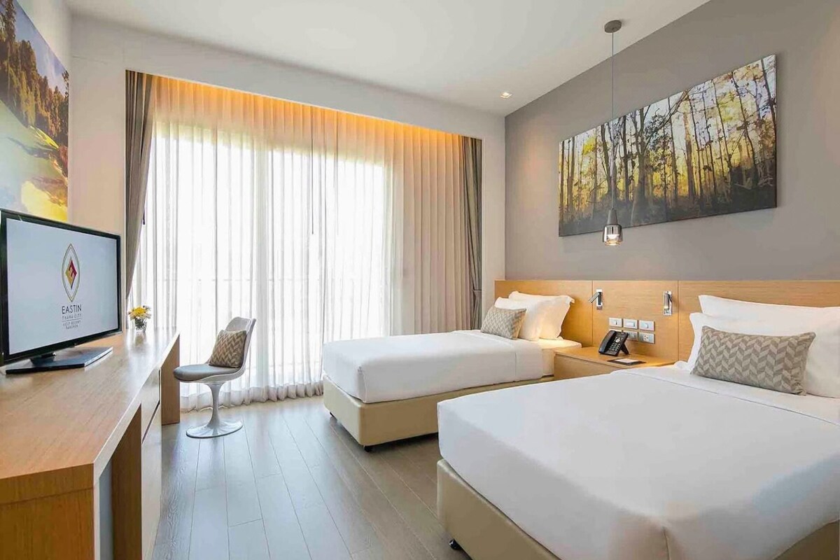 Une chambre d’hôtel avec deux lits, un bureau avec un ordinateur, une chaise et un tableau au mur.