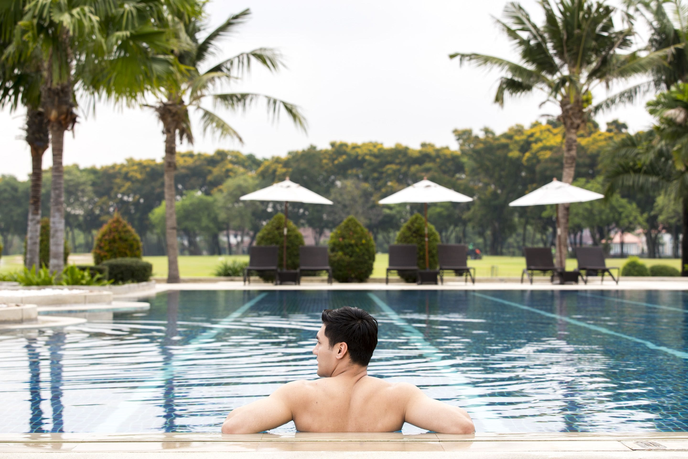 A man relaxing in a swimming pool with palm trees and lounge chairs in the background.