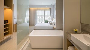A modern hotel room with a large bathtub, a bed with white linens, a green chair, and a view of the city through large windows. - Eastin Thana City Golf Resort Bangkok (Bang Phli)