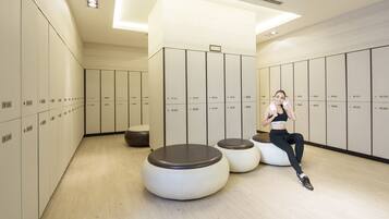 A modern locker room with multiple lockers, a seating area, and a person using a phone.