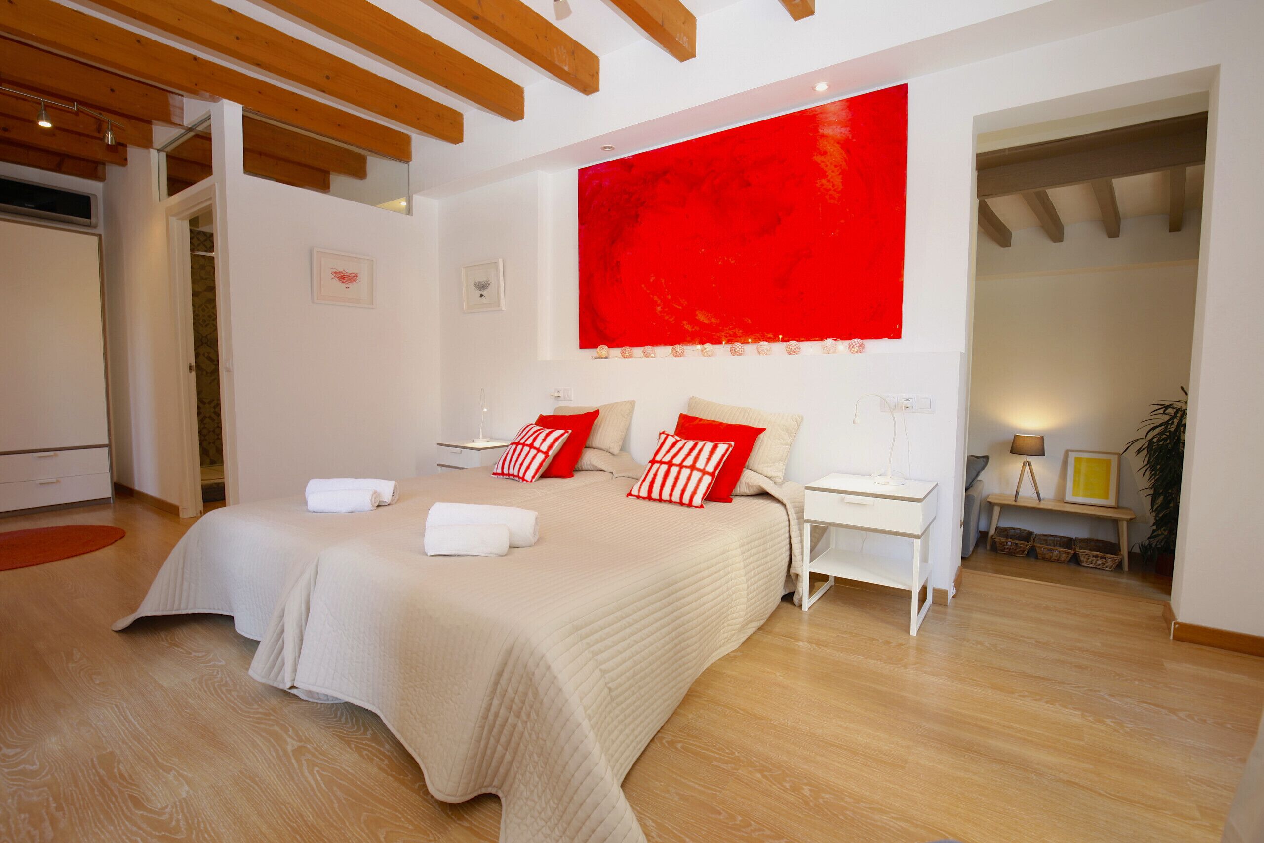 Une chambre à coucher moderne avec un grand lit, un mur d’accent rouge et des poutres en bois au plafond.