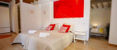 Une chambre à coucher moderne avec un grand lit, un mur d’accent rouge et des poutres en bois au plafond.