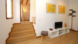 Escadaria que leva a uma sala de estar com televisão, obras de arte e uma placa indicativa.