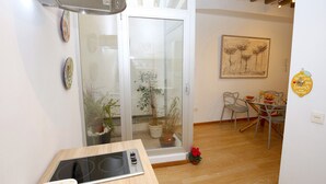Uma cozinha moderna com fogão embutido, porta de vidro que dá para uma varanda com plantas em vasos e uma área de jantar com mesa e cadeiras.
