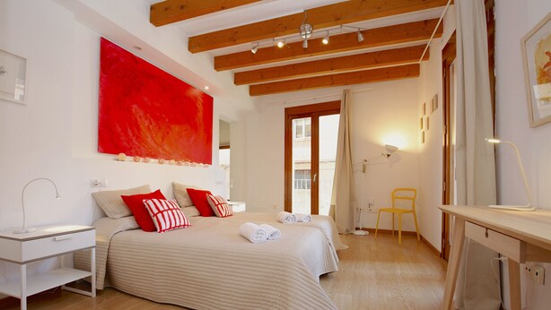 Quarto com cama, mesa de cabeceira, abajur e um quadro vermelho grande na parede.