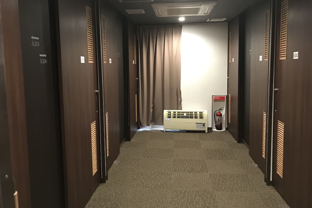 Pasillo de hotel con puertas de madera, numeradas A205 y A206, un extintor y un techo con iluminación empotrada.