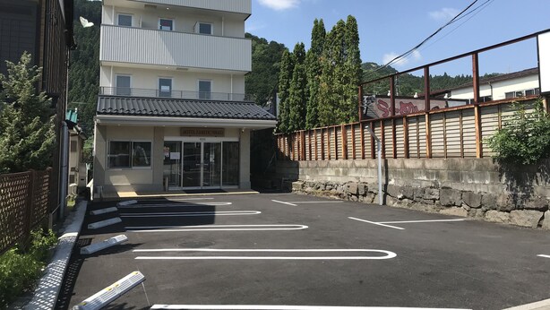 A hotel with a multi-story building, a parking lot with marked spaces, and a stone wall with a fence. - Hotel Famitic Nikko (Nikko)