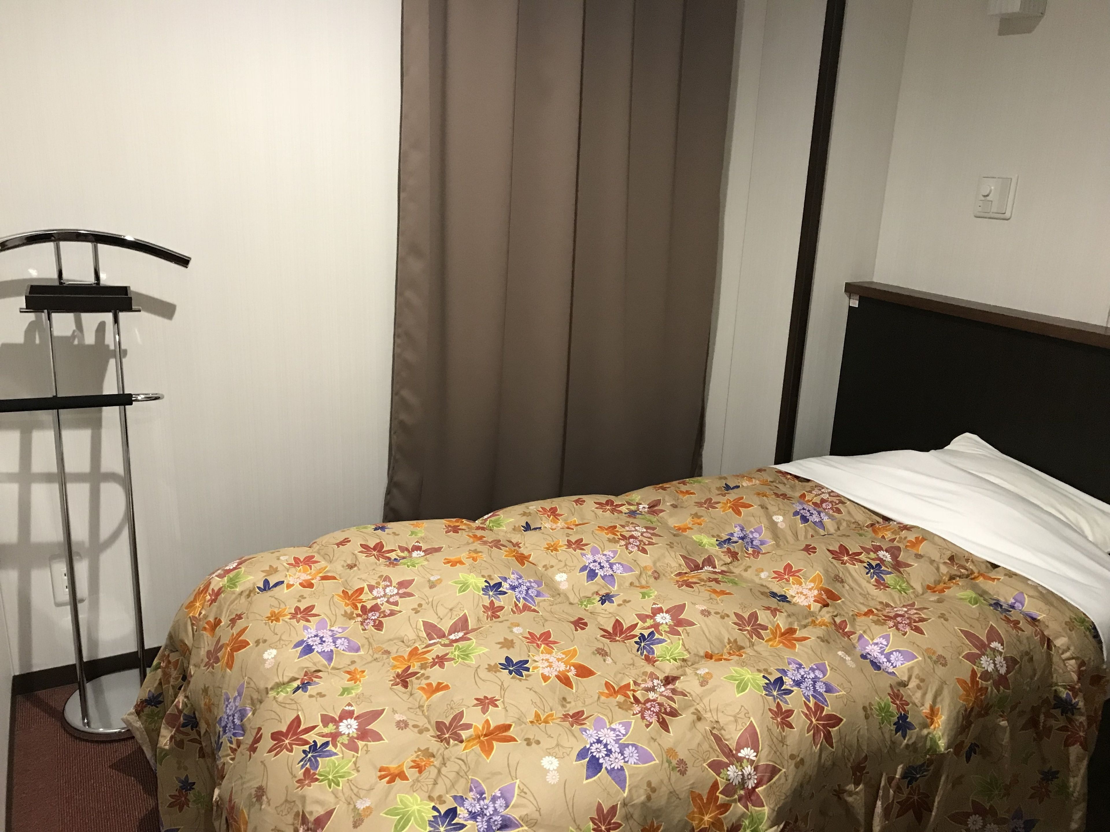 Un dormitorio con una colcha estampada de flores, un soporte de metal y una cortina.