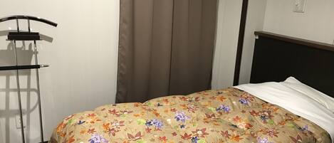 Un dormitorio con una colcha estampada de flores, un soporte de metal y una cortina.