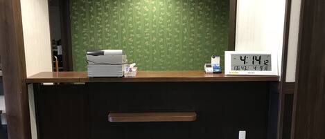 A reception desk with a digital clock displaying 14:14, a scale, and a printer.