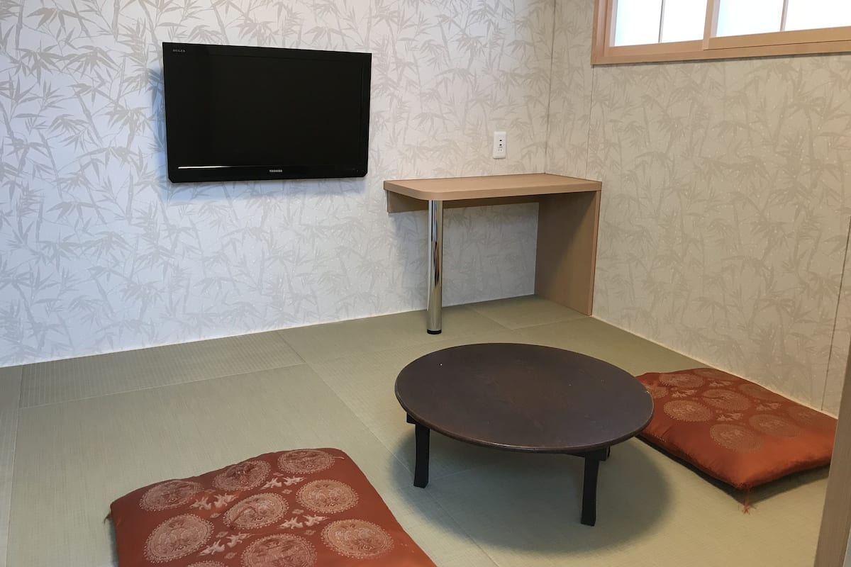 Una habitación con una televisión de pantalla plana montada en la pared, una pequeña mesa de madera y dos bancos acolchados.