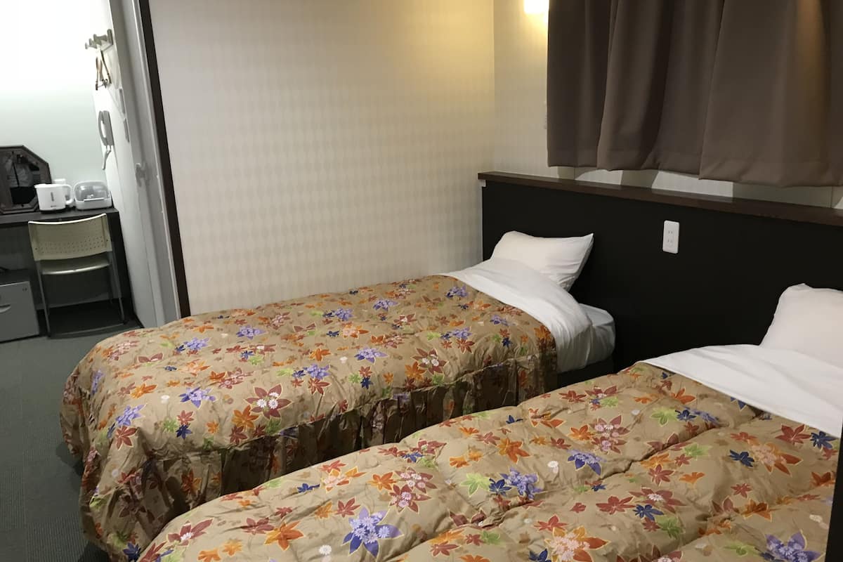 Habitación de hotel con dos camas, cada una con ropa de cama floral, un escritorio con hervidor y una silla.