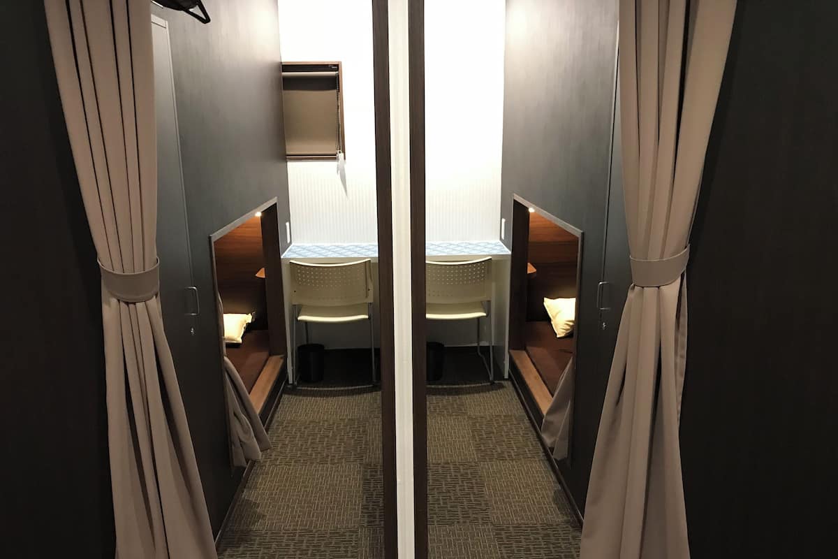Reflejo de una habitación con cama, una silla, una mesita y un ventanal.