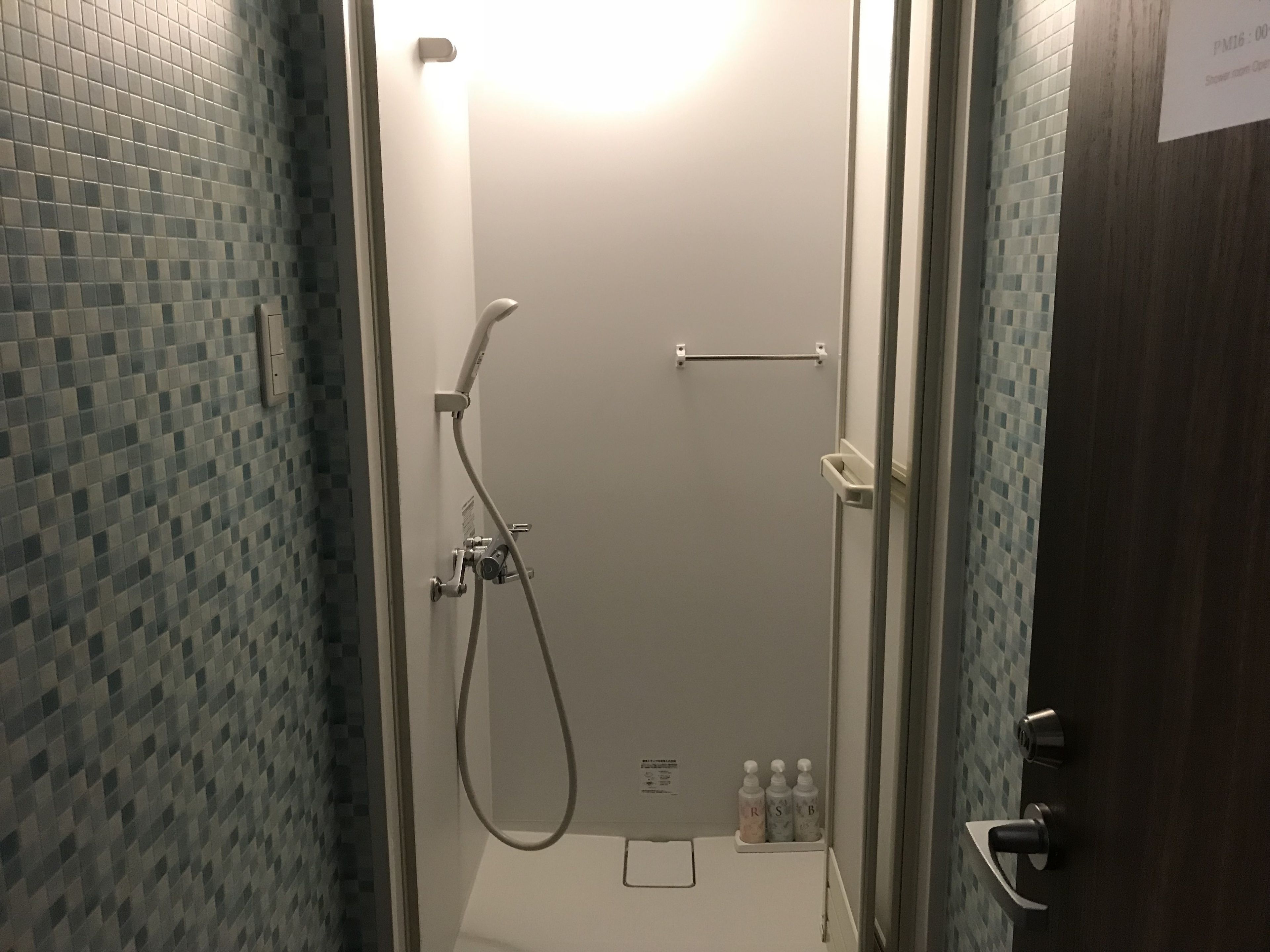 A shower area with a tiled wall, a handheld showerhead, a towel rack, and a soap dispenser.