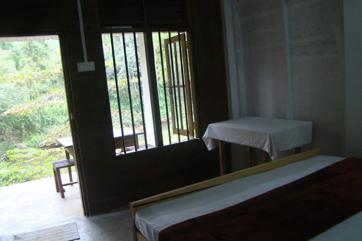 A room with a bed, a small table, and a window with a view of greenery.