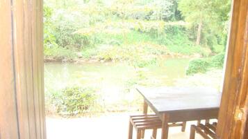 A wooden table and chairs outside a building with a view of a pond and greenery.