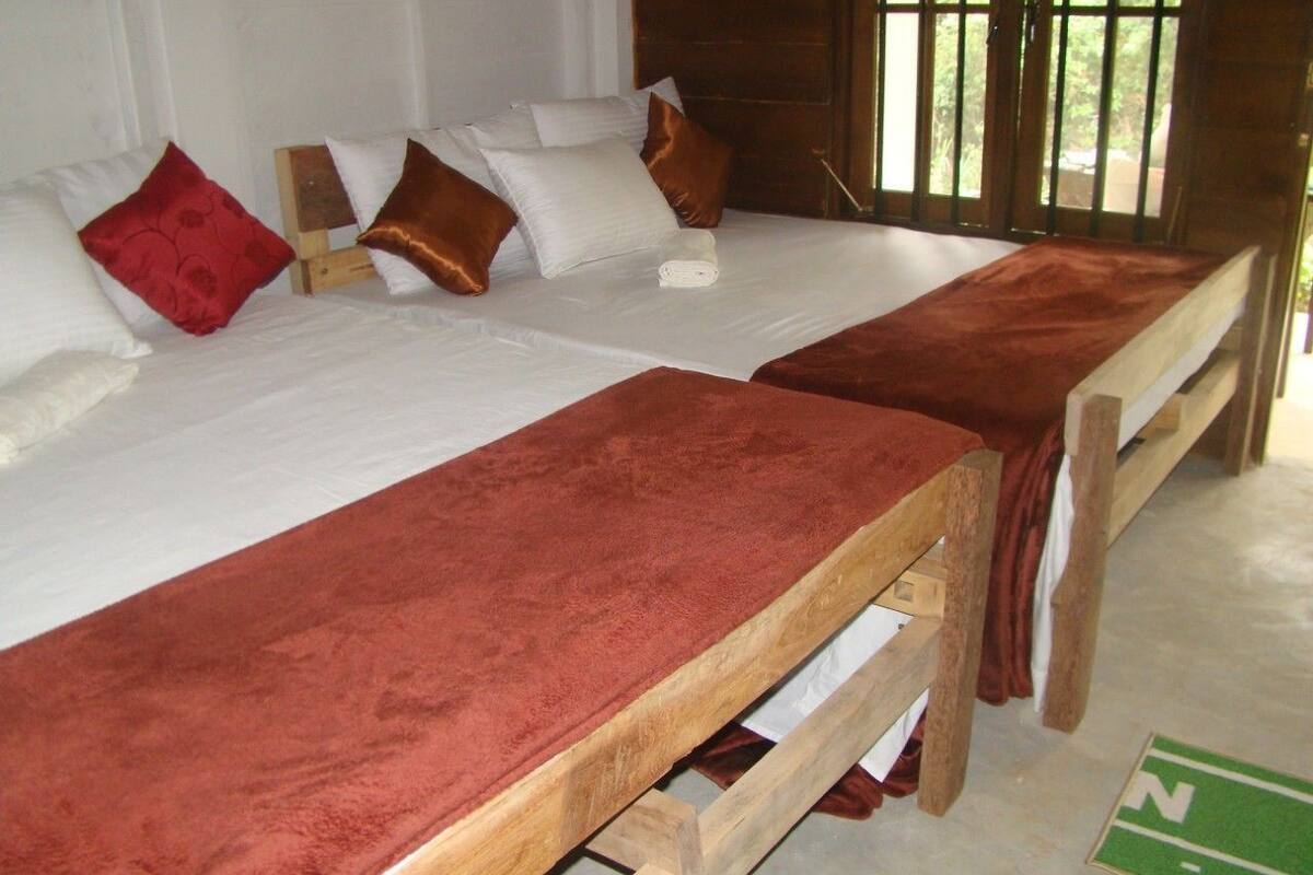 A room with two wooden beds, white bedding, and a red blanket.