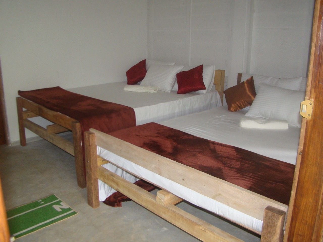 Ein Zimmer mit zwei Holzbetten, jeweils mit weißer Bettwäsche und roten Kissen.