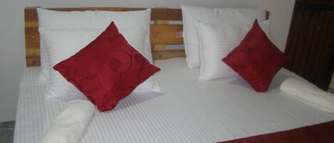 Una cama con ropa de cama blanca y dos almohadas rojas, una toalla blanca enrollada y una manta roja.