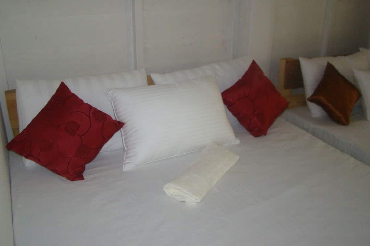 A hotel room with a neatly made bed, white linens, and red and brown pillows.