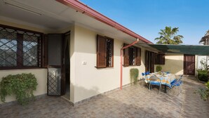 Un espacio cubierto con patio, que incluye una mesa, sillas, una puerta y ventanas con contraventanas.