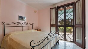 Un dormitorio con cama, mesita de noche, lámpara de pared y ventana con vistas.