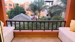 A balcony with two white cushioned sofas and two white chairs, overlooking a street with buildings and palm trees. - South Marina Fiorita house (Hurghada)